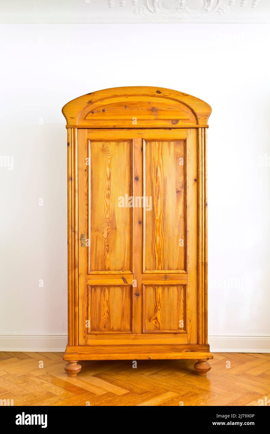 Restored vintage furniture: antique wooden wardrobe against the white wall of an old building with parquet flooring and stucco plastering, copy space. Stock Photo
