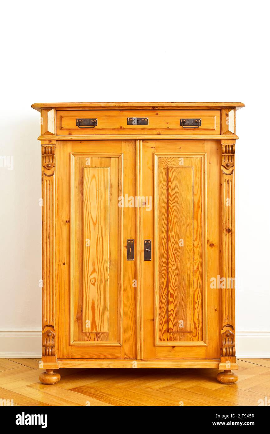 Restored vintage wooden cabinet or cupboard against the white wall of an old building with parquet flooring and stucco plastering, copy space. Stock Photo