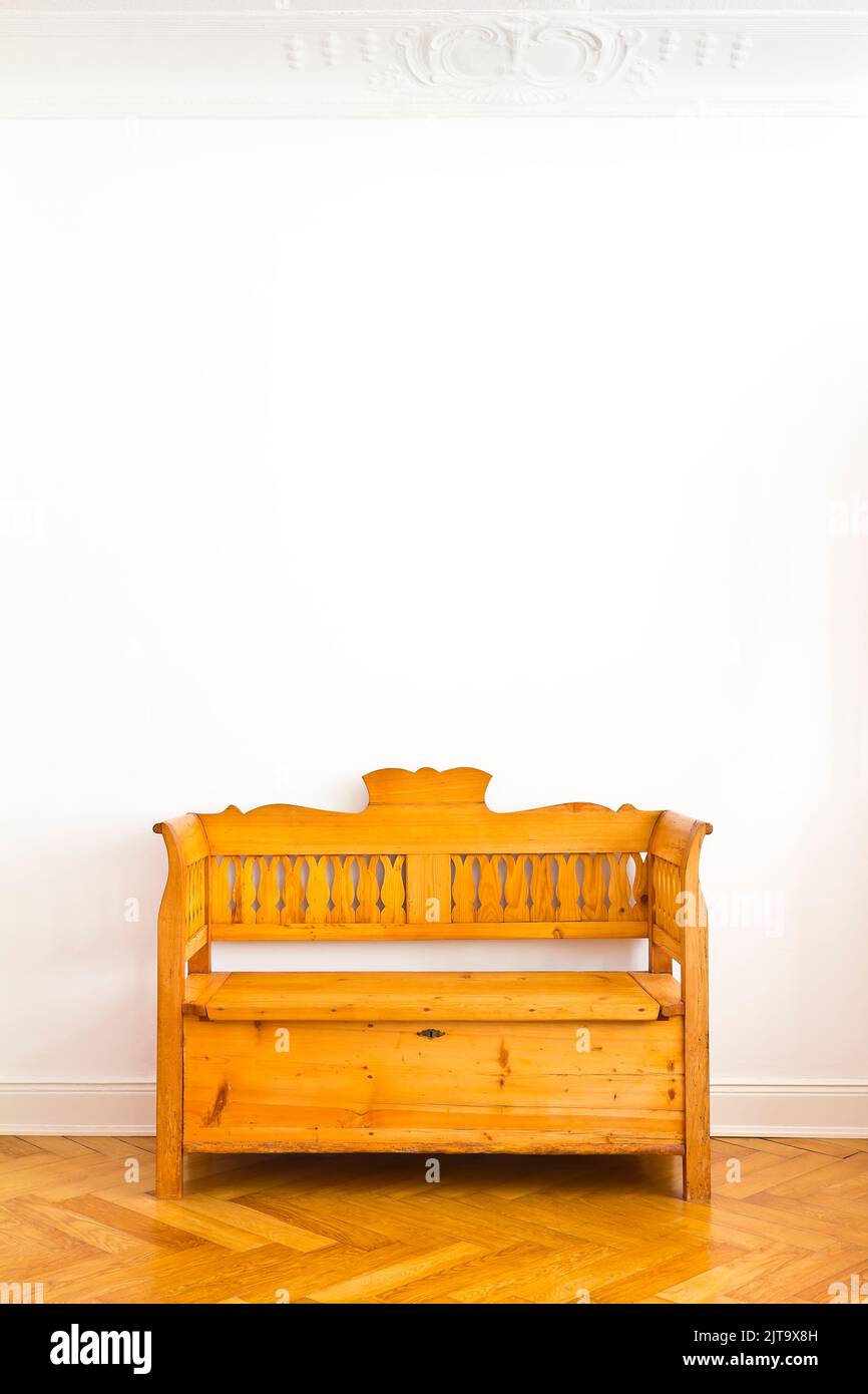 Old wooden box bench with storage space unter the seat, circa 1880, against the white wall of an old building with parquet flooring, copy space. Stock Photo
