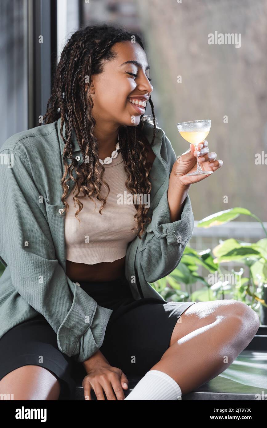 Smiling african american woman holding cocktail while sitting on ...