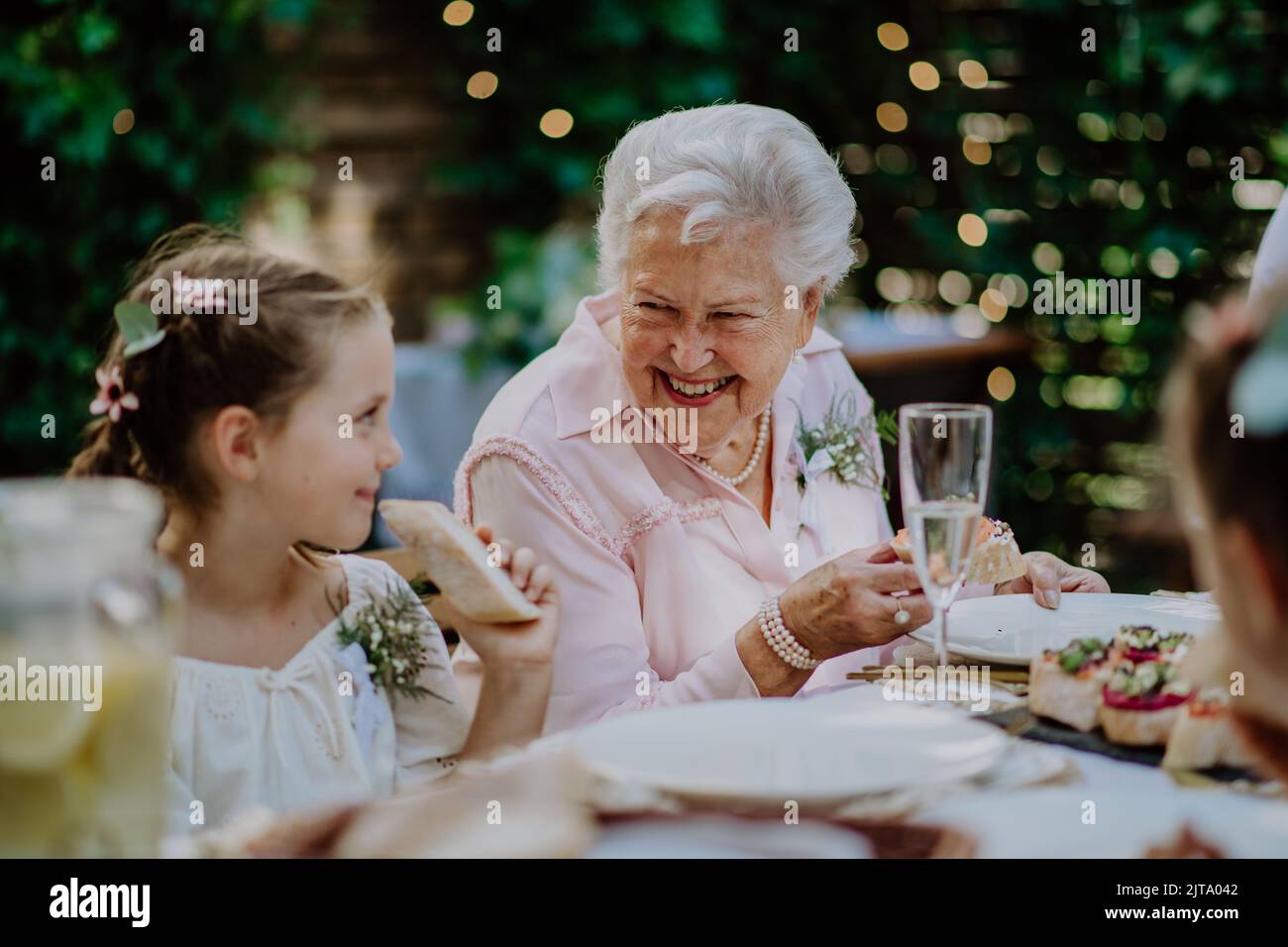 Wedding guests sitting by table, eating and drinking at reception outside in the backyard Stock