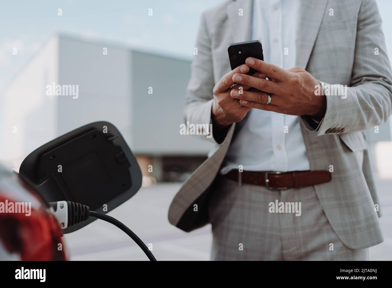 Man holding smartphone while charging car at electric vehicle charging station, closeup. Stock Photo