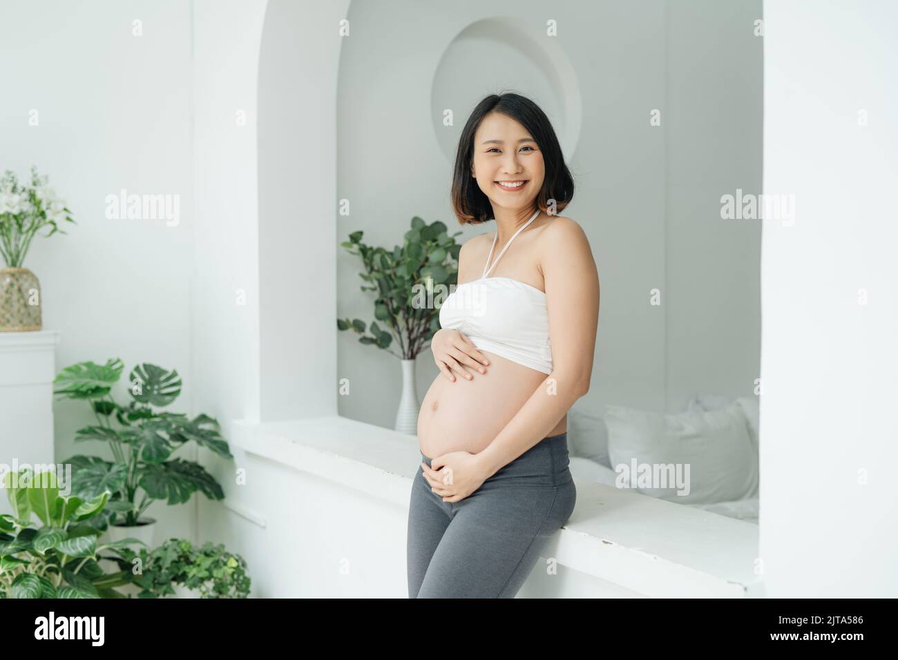 joyful pregnant woman with hands on belly posing at camera Stock Photo