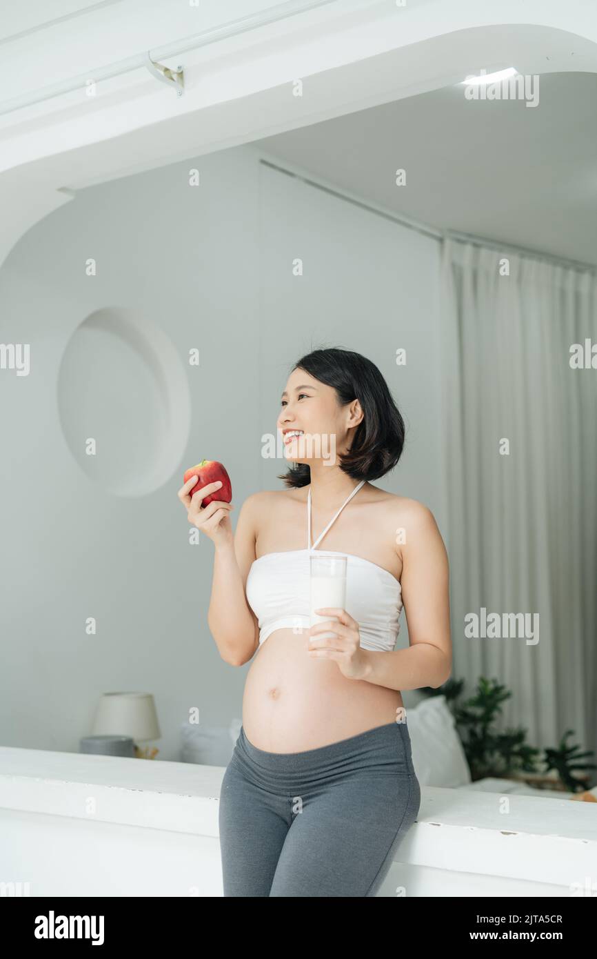 Pregnant Woman holding her pregnant belly and get a glass of milk and apple. Stock Photo