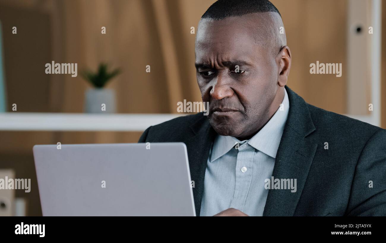 Upset frustrated African American adult old senior mature businessman elderly citizen man looking in laptop screen with sad lost failure suddenly Stock Photo