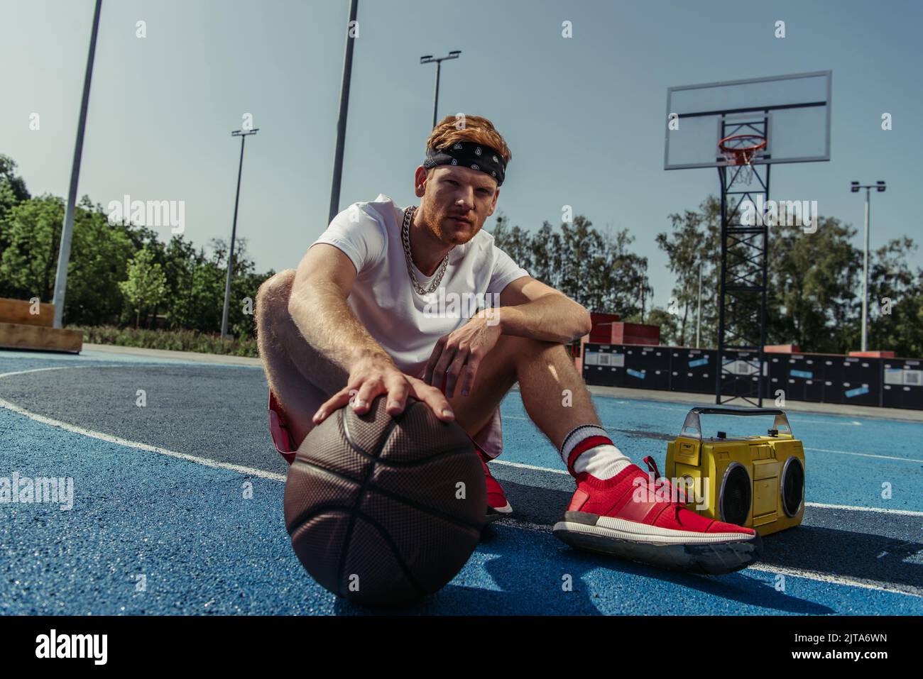 basketball player in sportswear and bandana sitting on court with ball