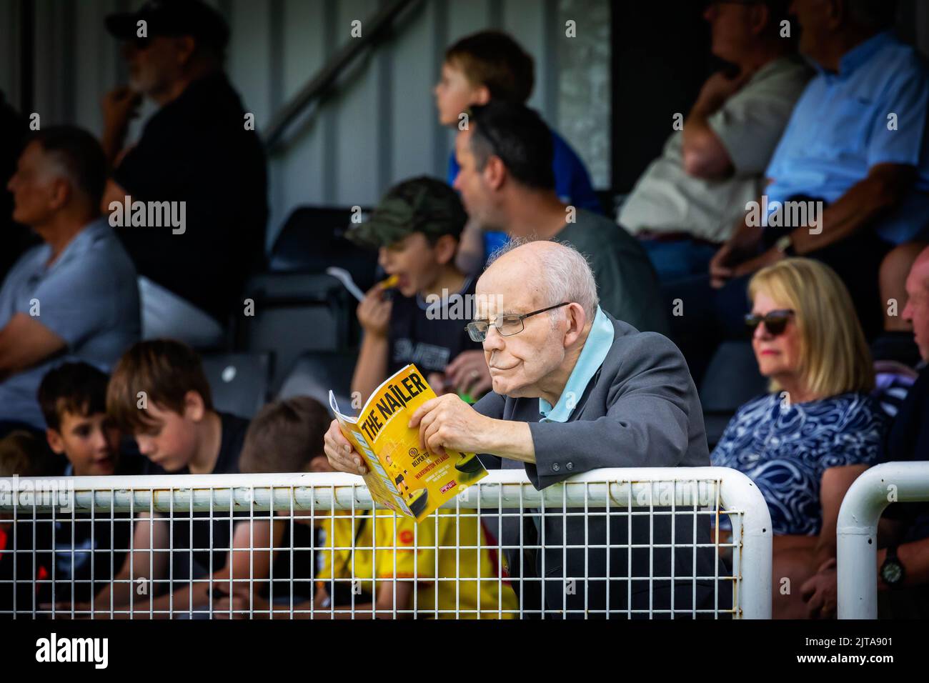 Mature gentleman leans against the barrier reading the programme at a Belper Town football match Stock Photo