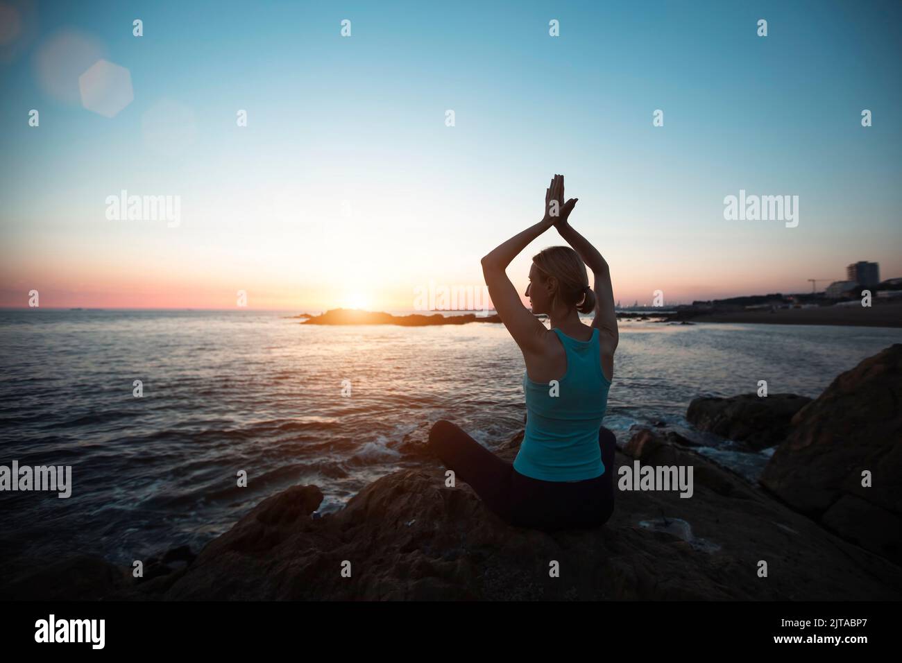 A middle-aged woman of athletic build does yoga, meditating on the ocean beach during a beautiful sunset. Stock Photo