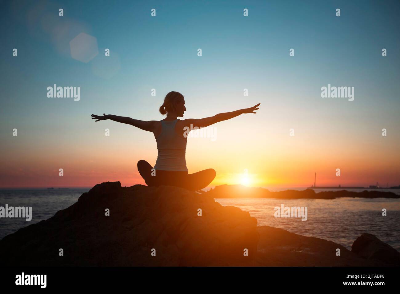 Silhouette women do yoga, meditate on the ocean during sunset. Stock Photo