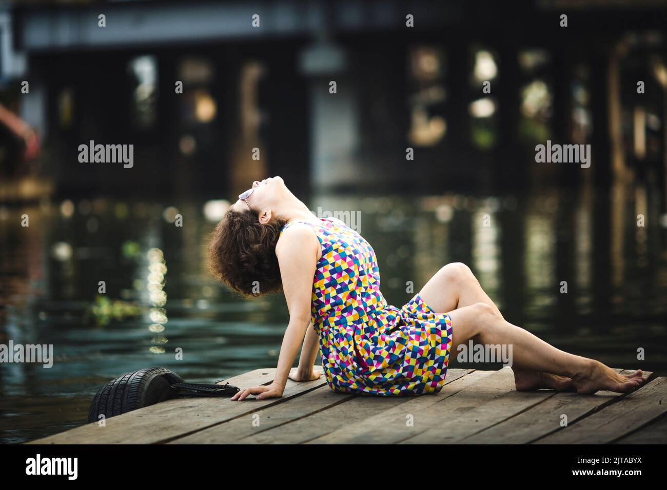 A fashionable Asian woman poses on a wooden river pier. Stock Photo