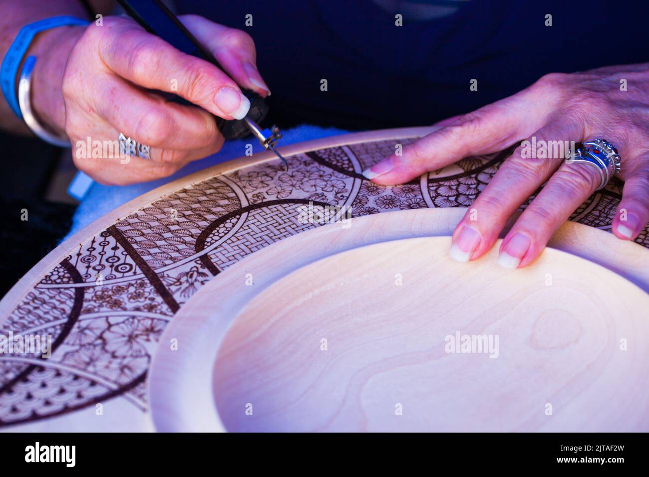 Abstract close-up of an artist handcrafting her artistic designs onto wood using a pyrography burner. Stock Photo