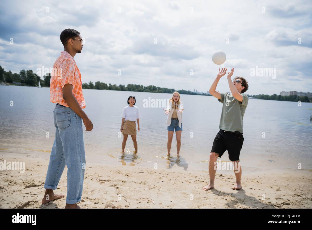 young man passing ball while playing beach volleyball with interracial friends Stock Photo