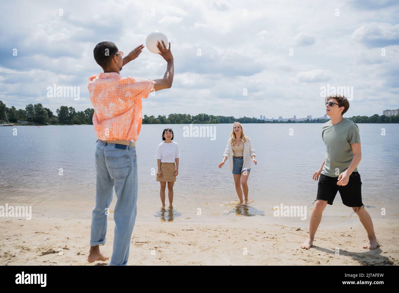 african american man passing ball while playing beach volleyball with multiethnic friends Stock Photo