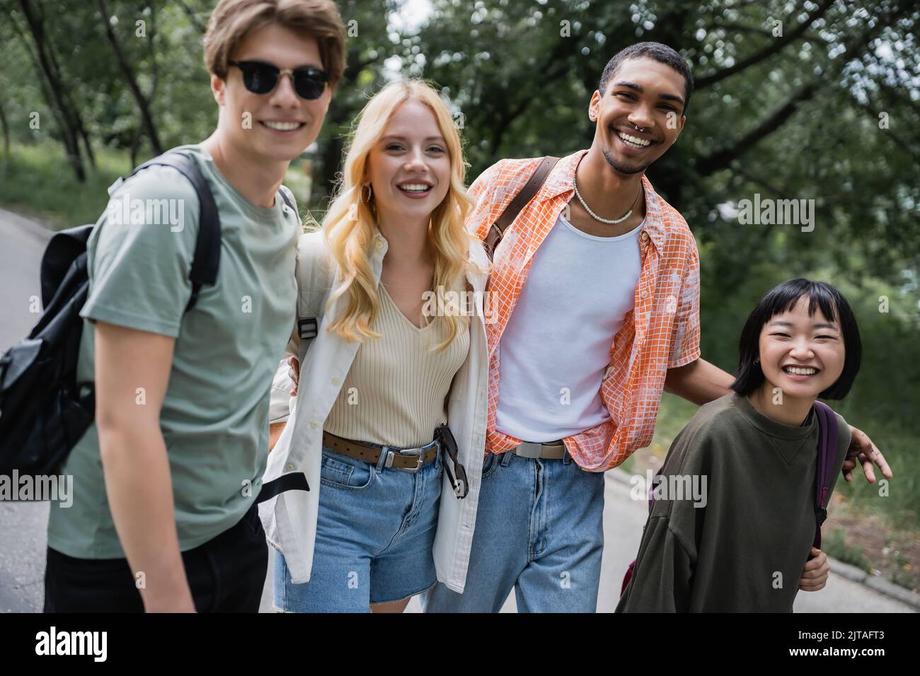 happy multicultural travelers with backpacks smiling at camera outdoors Stock Photo