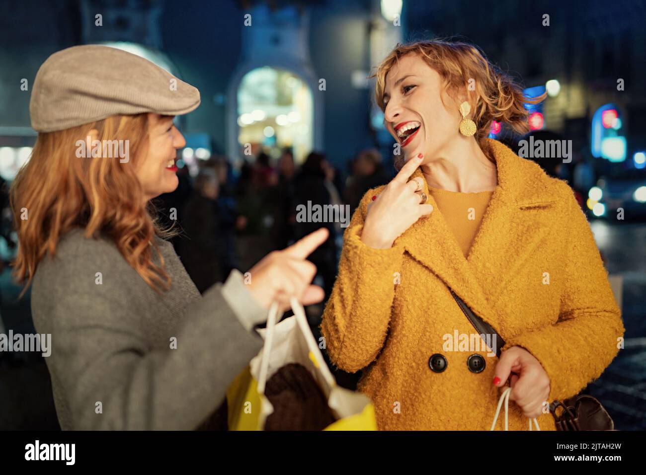 Two forty women talking and laughing carefree outdoors at Christmas market in the city center holding shopping bags - people lifestyle and holiday con Stock Photo