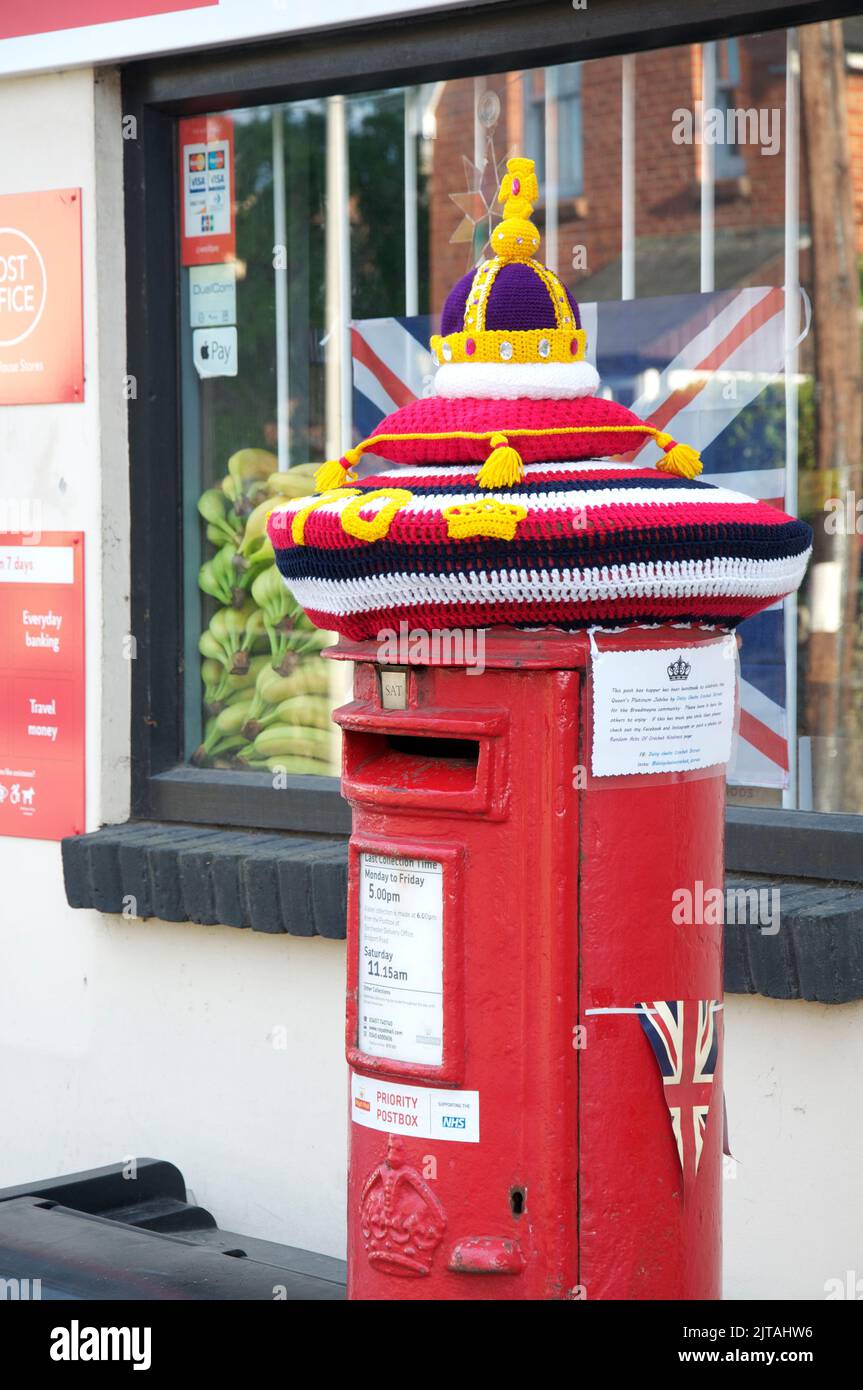 Quirky colourful handmade knitted woollen hat decorates a traditional red pillar box, celebrating the platinum Jubilee of Queen Elizabeth II. England. Stock Photo
