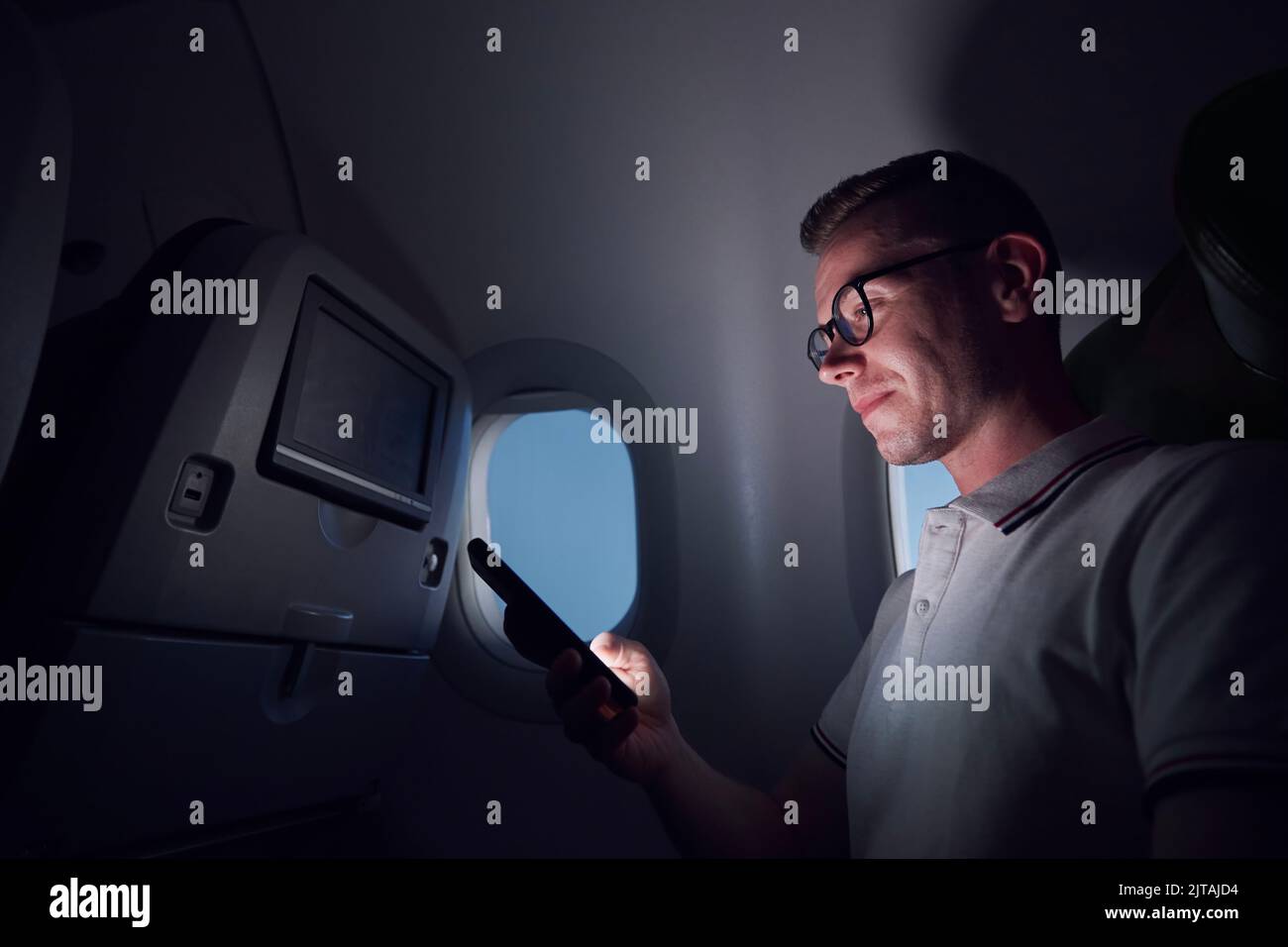 Man traveling by airplane. Passenger using phone during night flight. Stock Photo