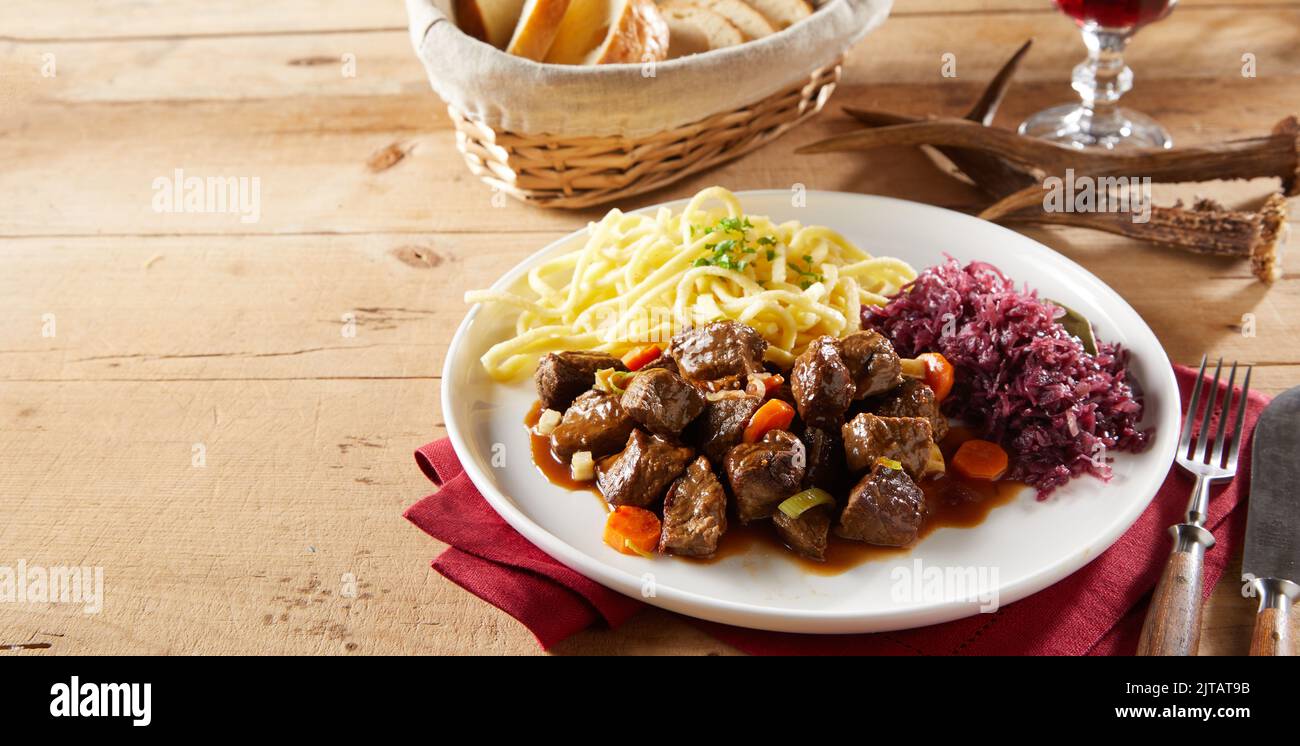 From above beef goulash with sauerkraut and spatzle pasta served on plate near deer antlers on wooden table during lunch in restaurant Stock Photo