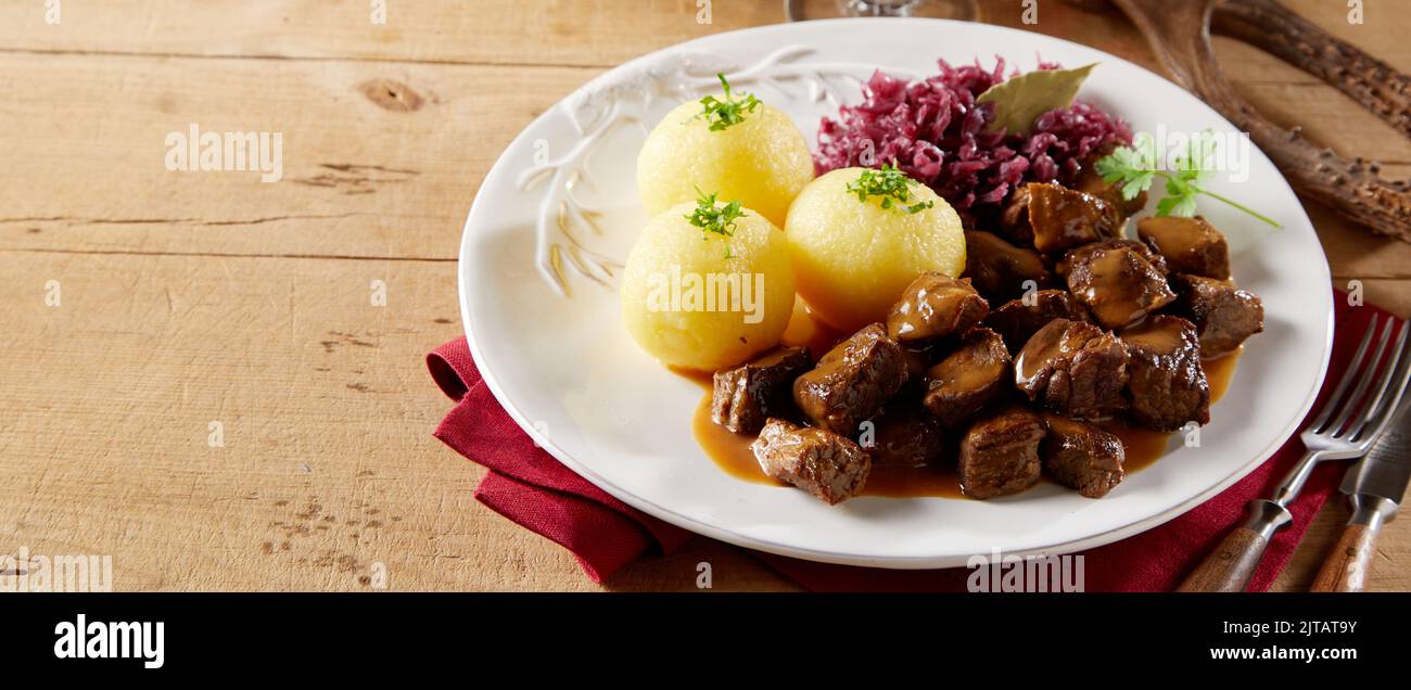 From above beef goulash and potato dumplings with sauerkraut served on ceramic plate on lumber table in restaurant Stock Photo