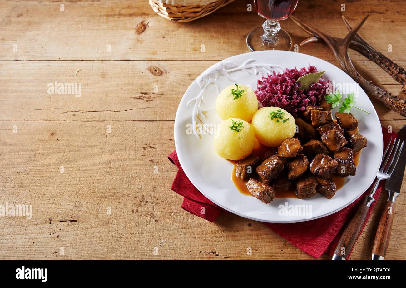From above beef goulash and potato dumplings with sauerkraut served on plate near cutlery and red wine on wooden table during lunch in restaurant Stock Photo