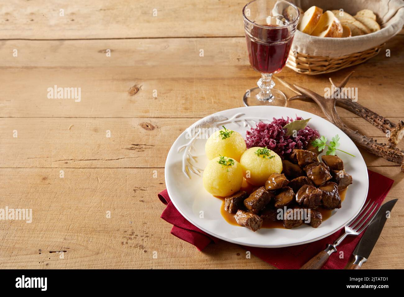 From above yummy beef goulash and potato dumplings with sauerkraut served on plate near red wine and bread on timber table with deer antlers and cutle Stock Photo