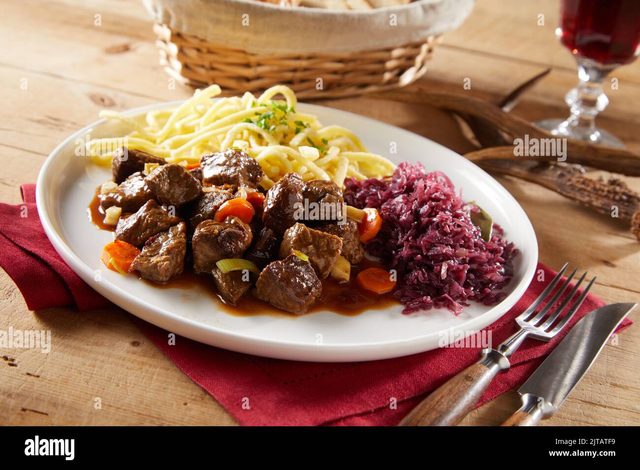 From above beef and vegetables goulash served for lunch with red cabbage sauerkraut and spatzle pasta on wooden table in restaurant Stock Photo