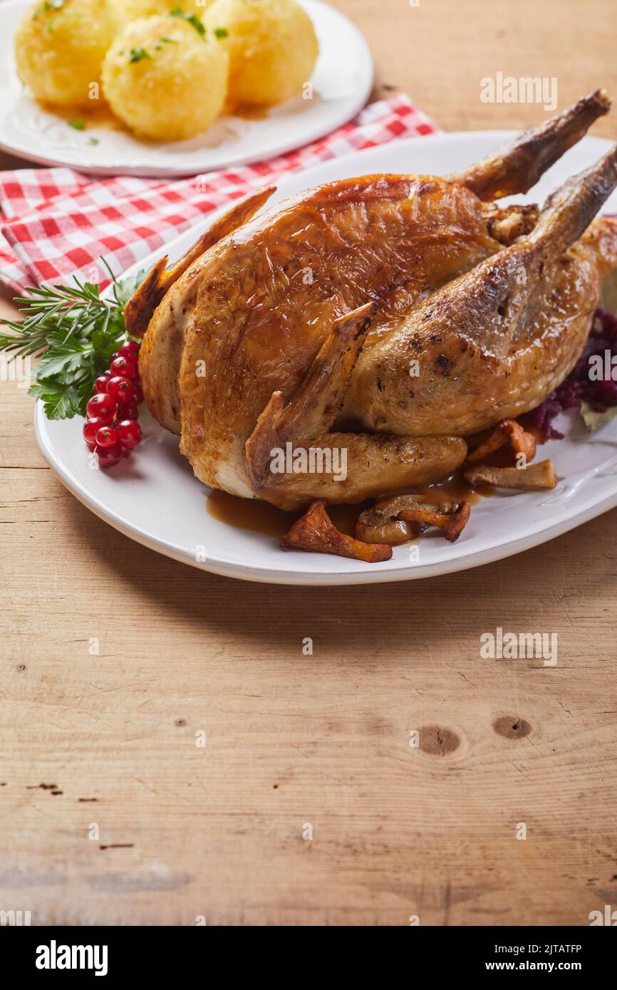 From above yummy roasted guinea fowl served on plate with herbs and red currant berries near napkin and tasty potato dumplings during lunch Stock Photo