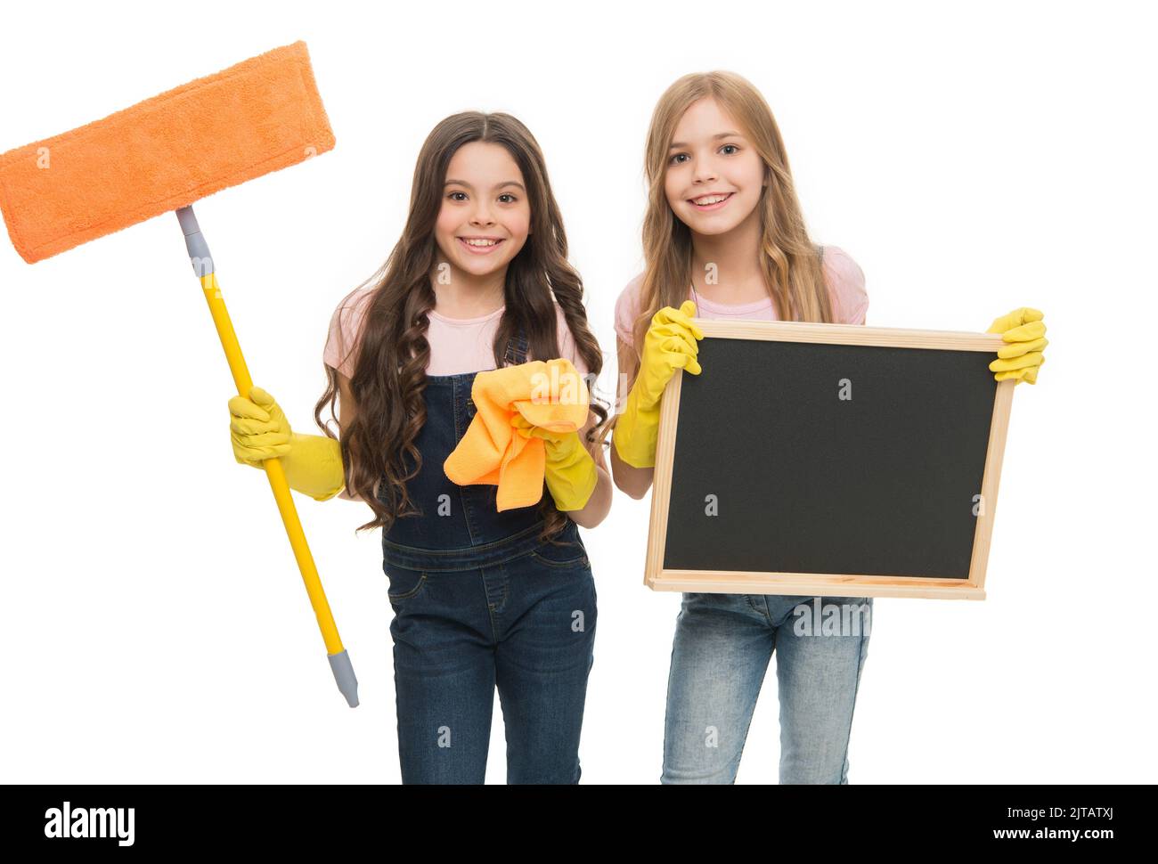 Having fun to work in team. Little schoolgirls enjoy doing cleaning work. Small cleaners in work gloves holding mop and blackboard. All kinds of Stock Photo