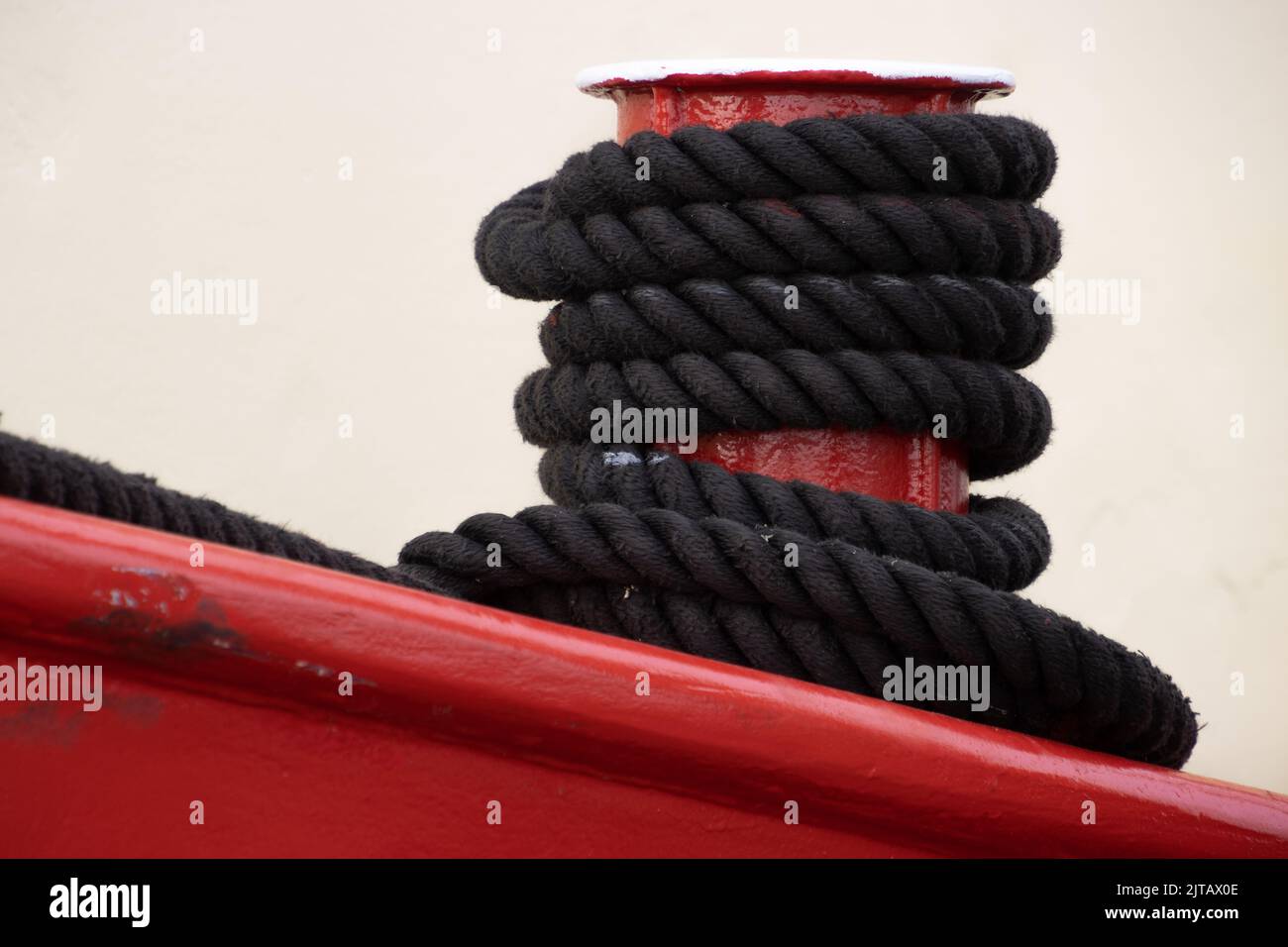 Black rope tied to a red metal mooring bollard Stock Photo