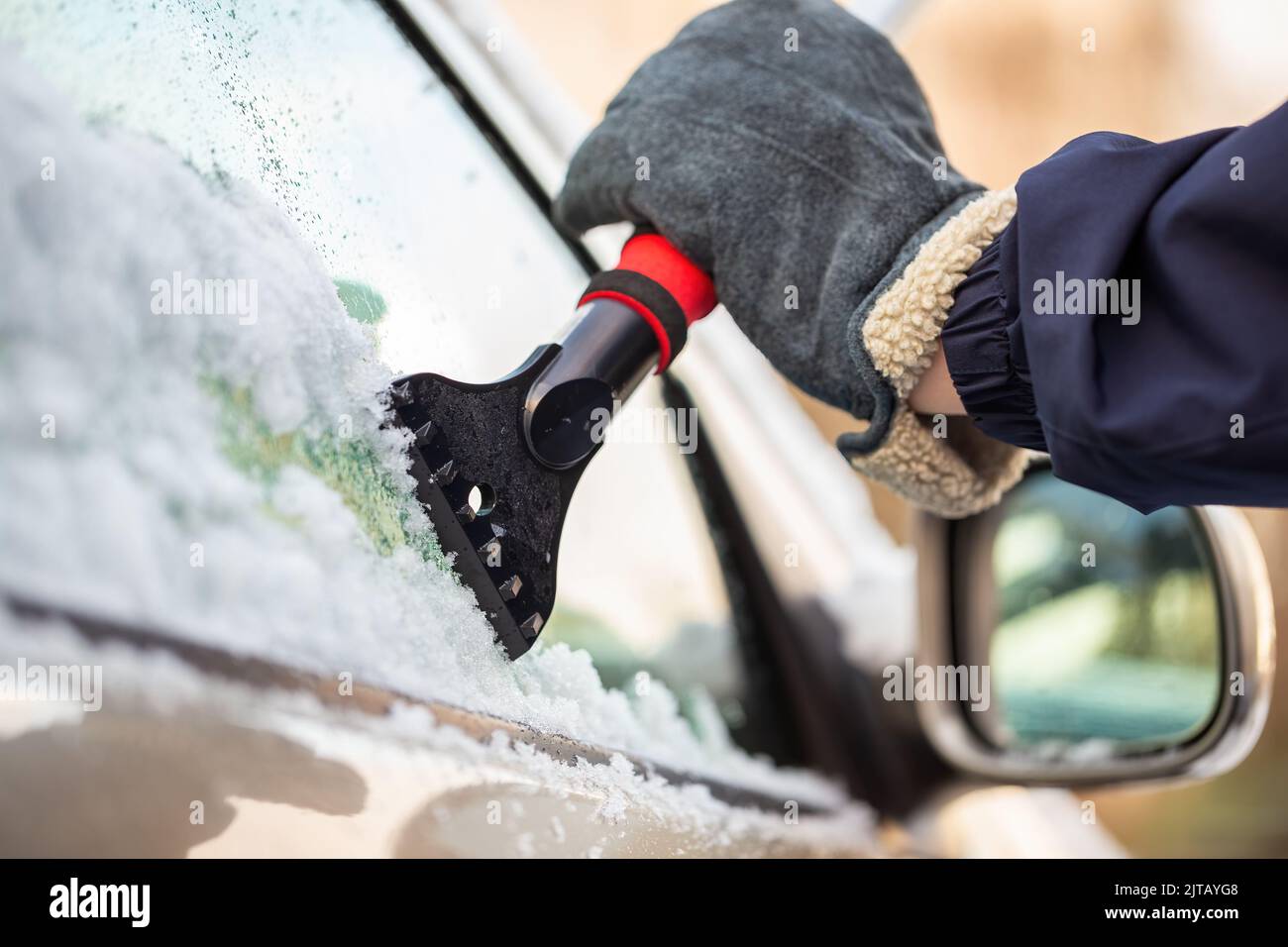 Hand in glove holding a snow scraper and removing ice from a car window