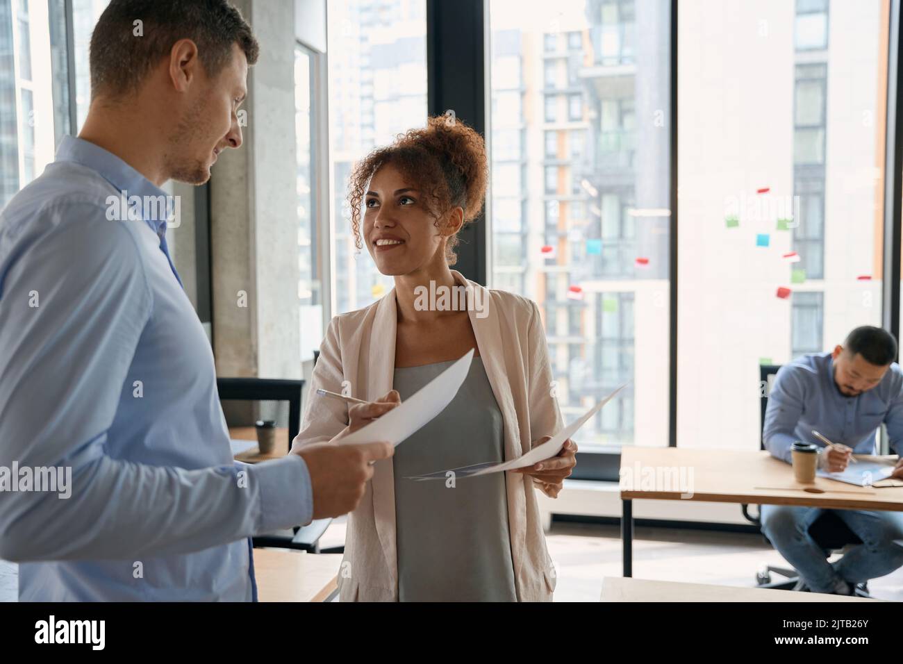 Joyful male and female discussing documents in modern coworking space ...