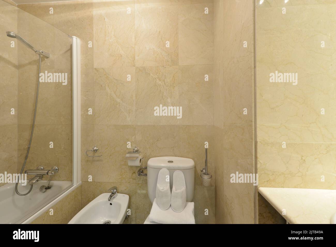 Bathroom with cream marble tiles, white toilets and shower cabin with glass partition Stock ...
