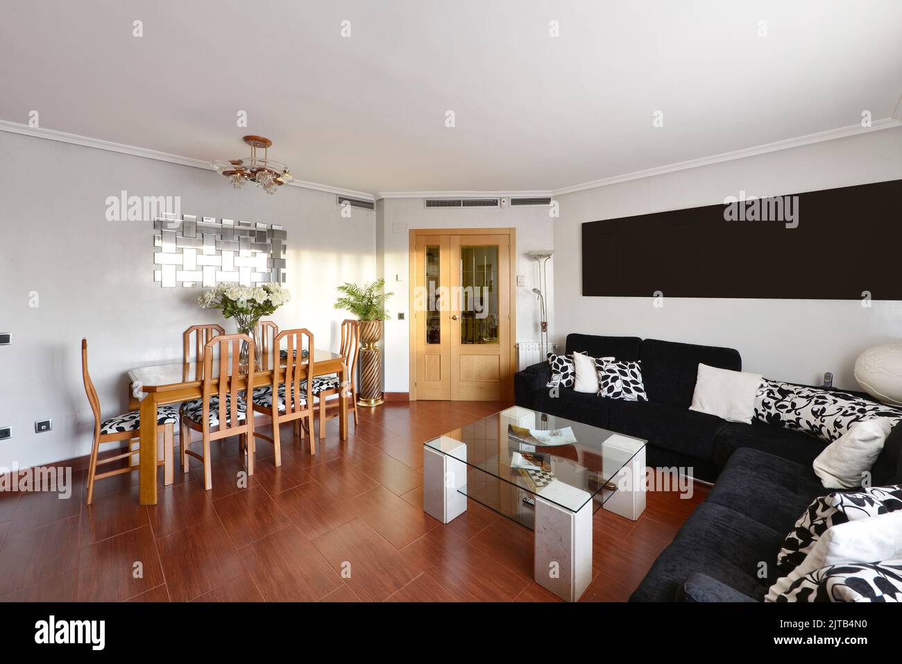 Living room of a residential home with a wooden dining table with matching chairs, a corner sofa covering two walls upholstered in black fabric and re Stock Photo