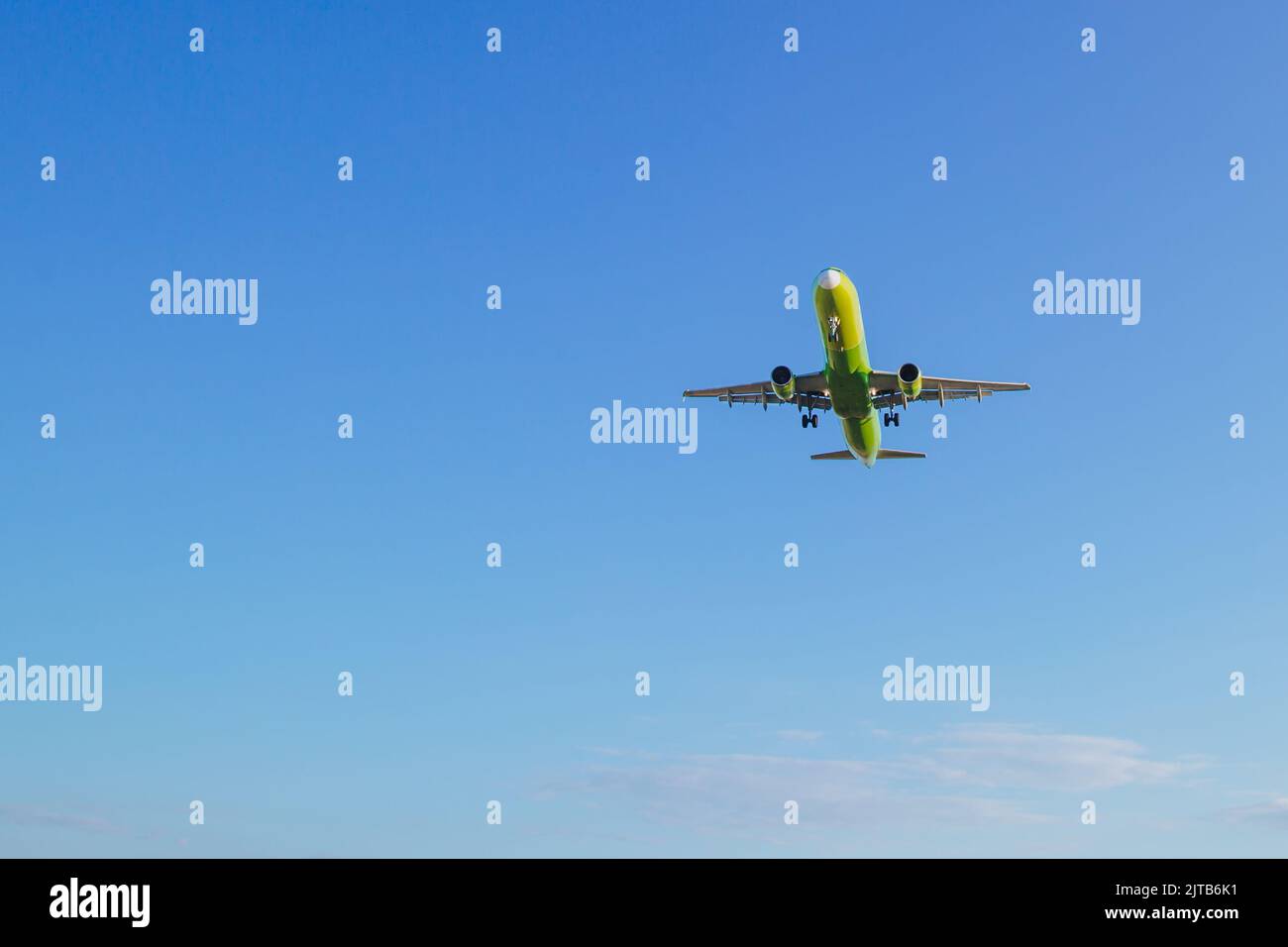 Passenger plane of yellow-green color flies in the blue sky, air transportation concept, population evacuation. Stock Photo