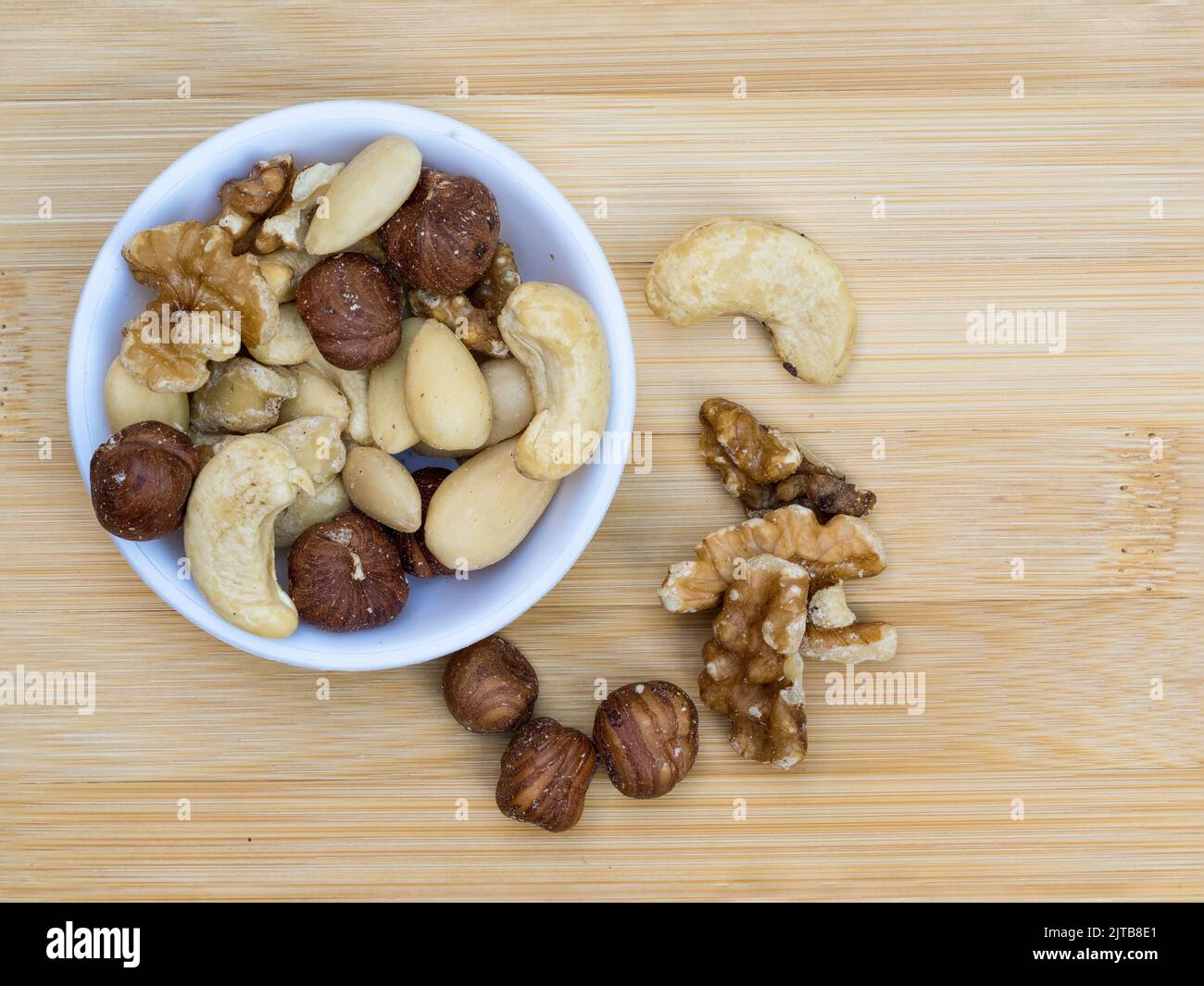 flat lay view mixed nuts in white porcelin bowl and overspill on a bamboo platter  dish Stock Photo