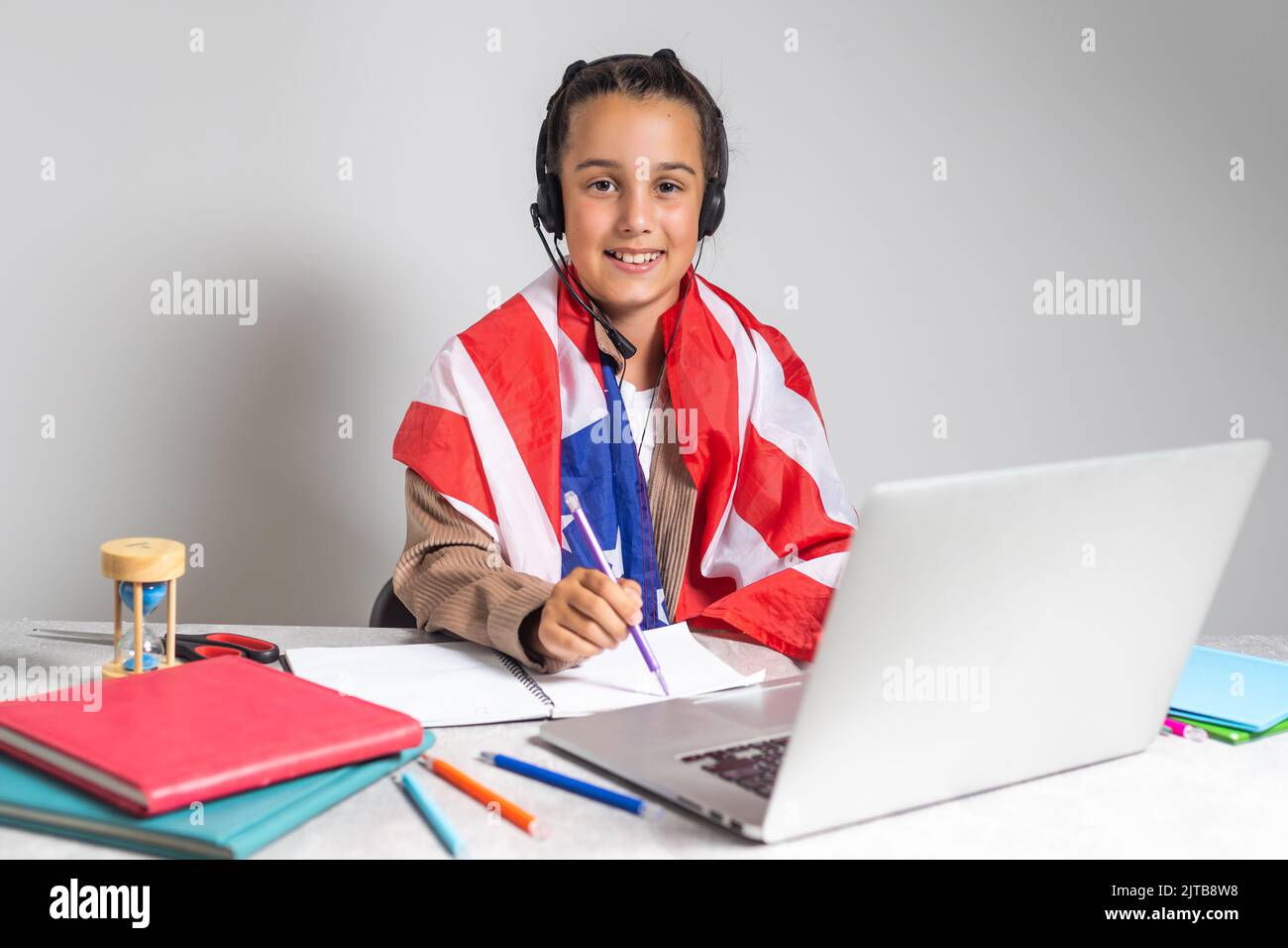beautiful pupil sitting at desk and study online with laptop against background with USA flag. Stock Photo