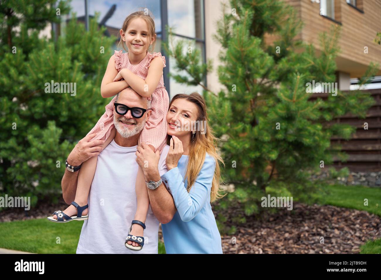 Happy young family stands in front of house with pines Stock Photo - Alamy