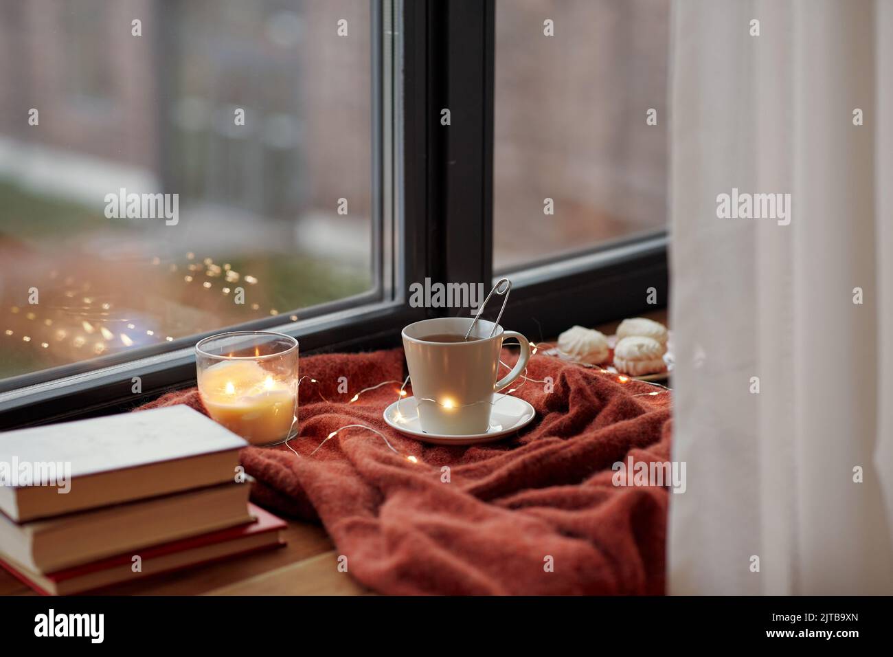 cup of tea, books and candle burning on windowsill Stock Photo