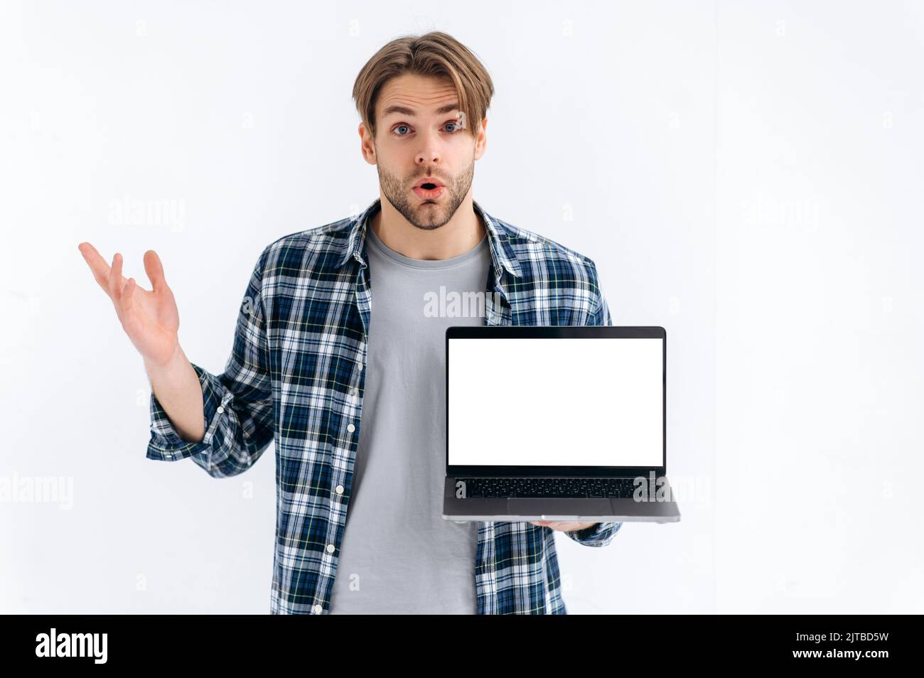 Confused stunned puzzled caucasian guy in casual wear, freelancer or student, holding an open laptop with empty mock-up space, stand on white isolated background, looks at camera in surprised Stock Photo