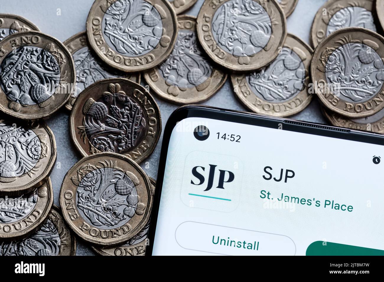 SJP application seen on smartphone screen placed on british pound coins. St. James's Place (SJP) is an Expert Financial Advice company. Stafford, Unit Stock Photo
