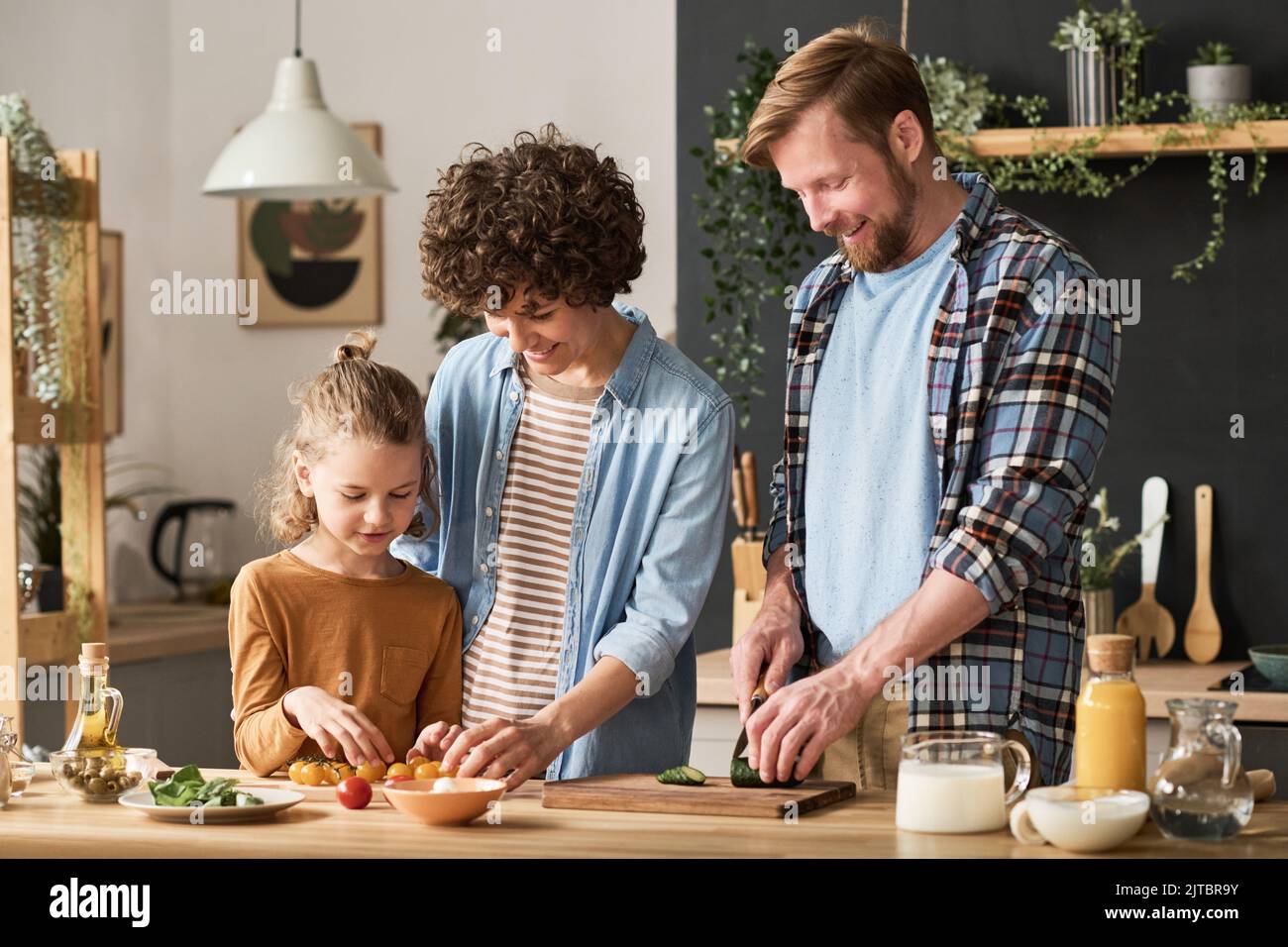 Happy parents teaching their son to prepare salad for dinner while standing at table in kitchen Stock Photo