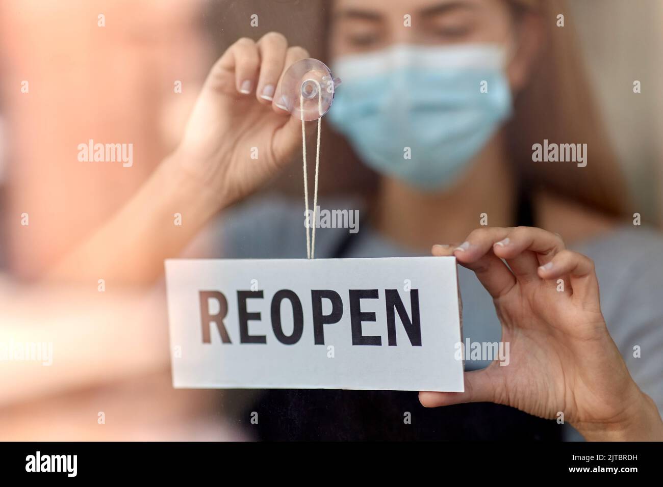 woman in mask with reopen banner on door glass Stock Photo