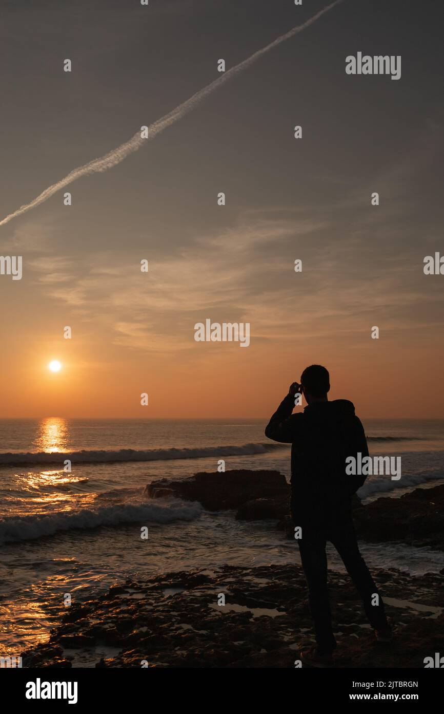 A silhouette of a man watching scenic sunset over the Atlantic ocean in ...