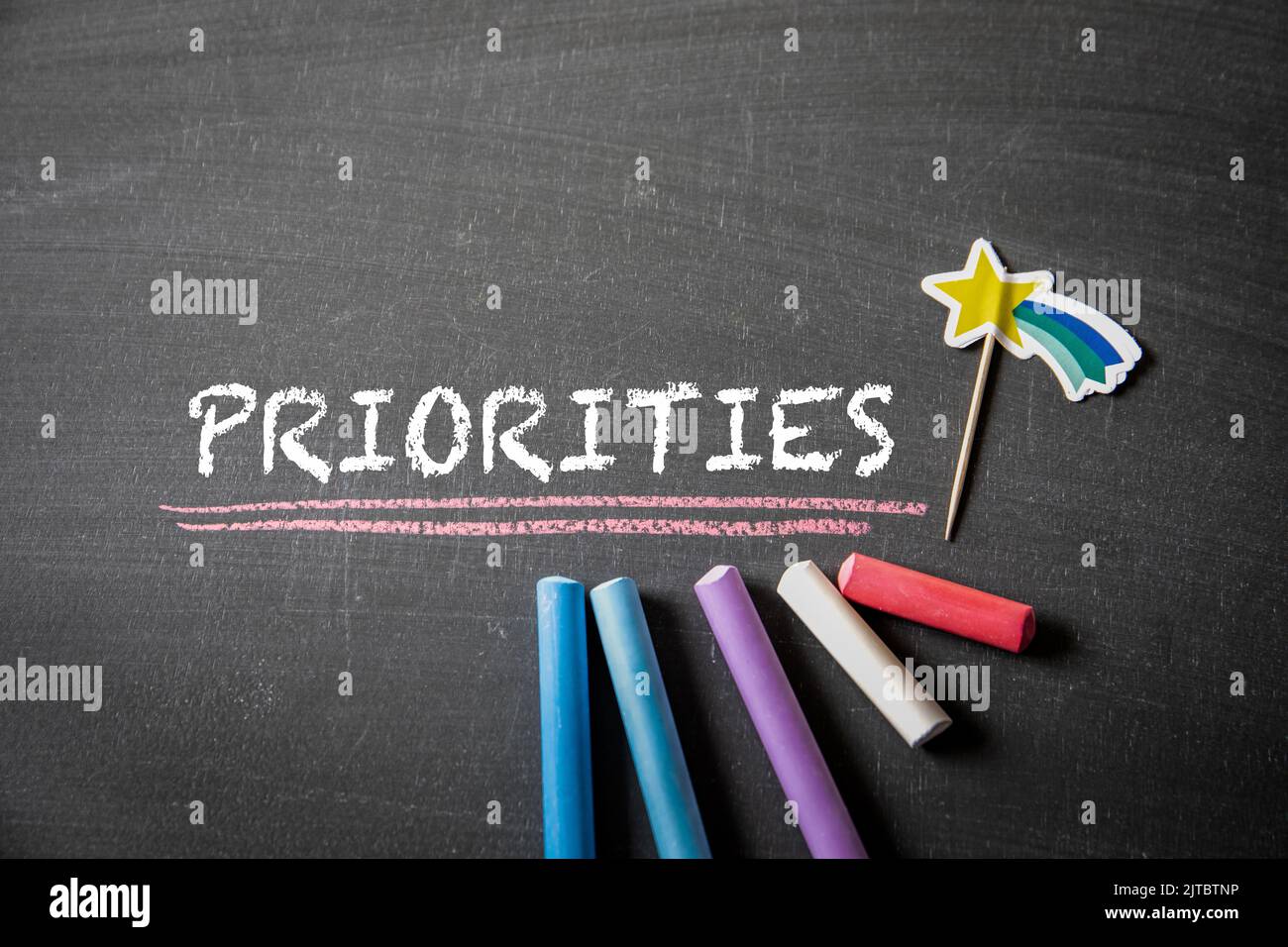 PRIORITIES. Text and colored pieces of chalk on a blackboard background. Stock Photo