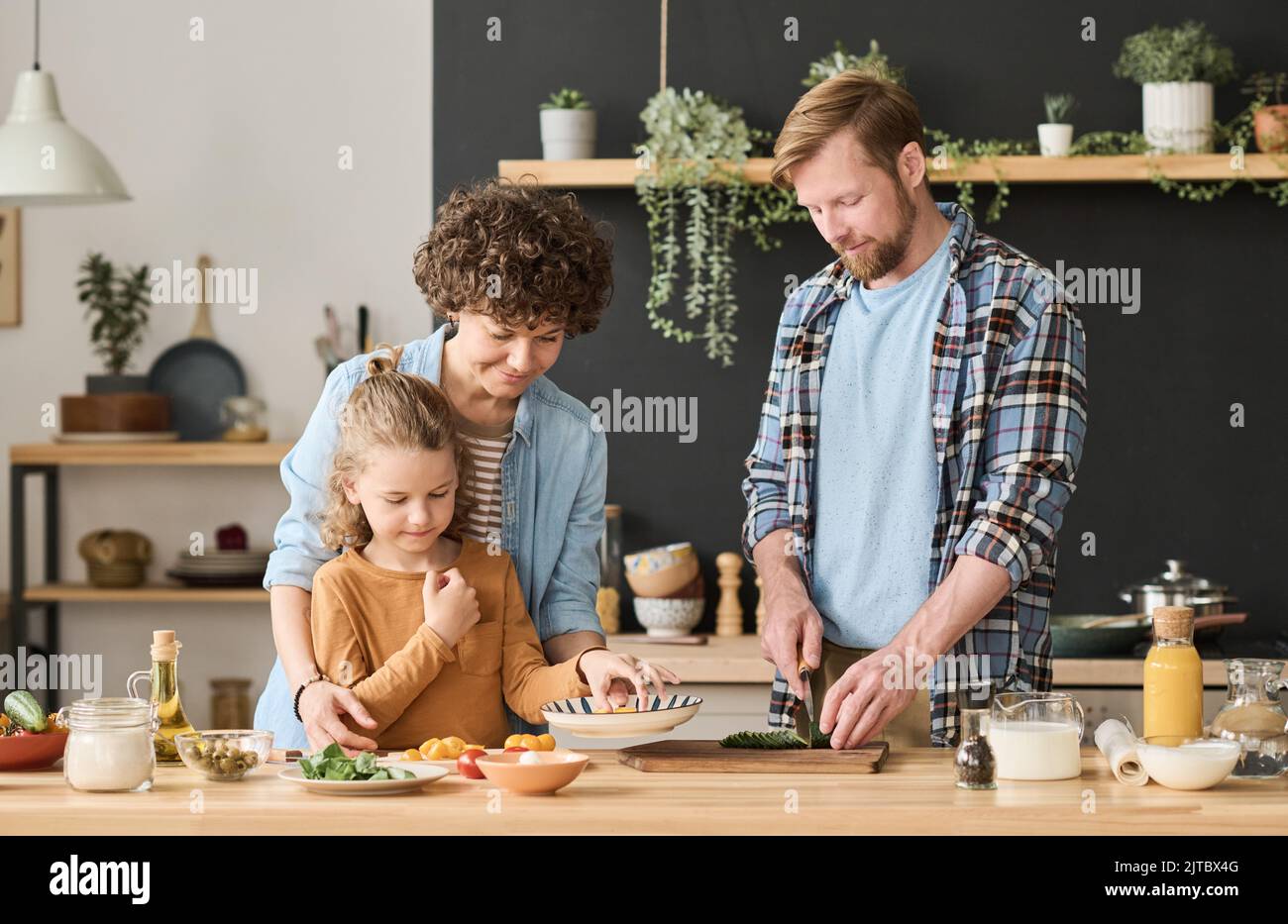 Young parents preparing dinner at table in kitchen together with their child Stock Photo