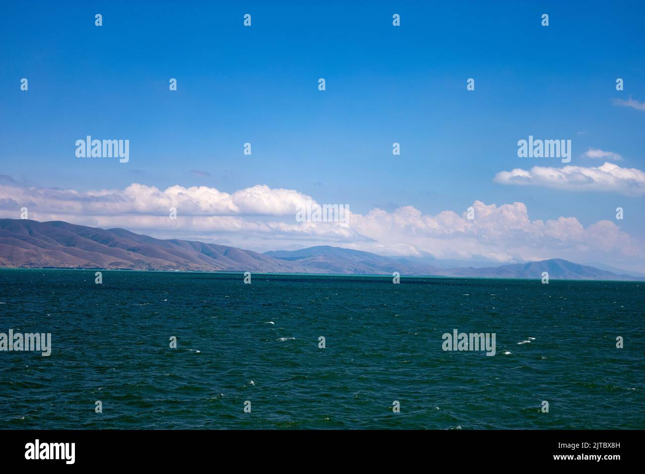 Lake Sevan partially colored in turquoise on a windy day, with mountains in the background in summer Stock Photo
