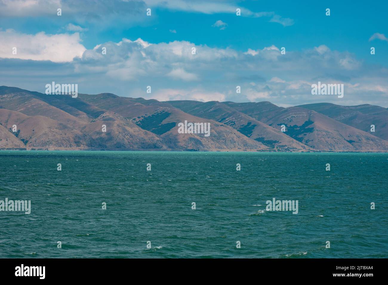 Lake Sevan partially colored in turquoise on a windy day, with mountains in the background in summer Stock Photo
