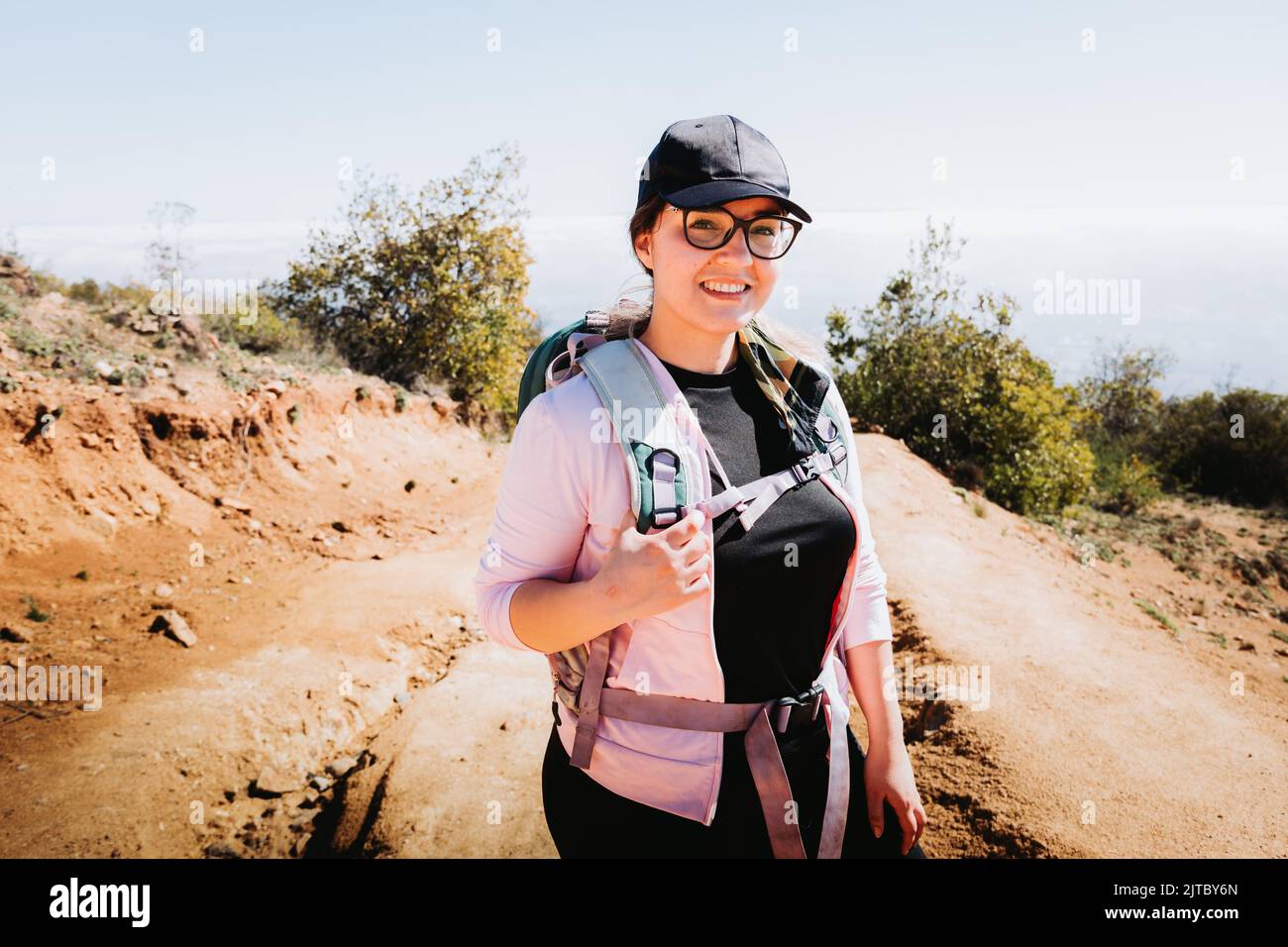 Young latin plus size woman with backpack on, climbing a hill and hiking in a beautiful landscape. Stock Photo