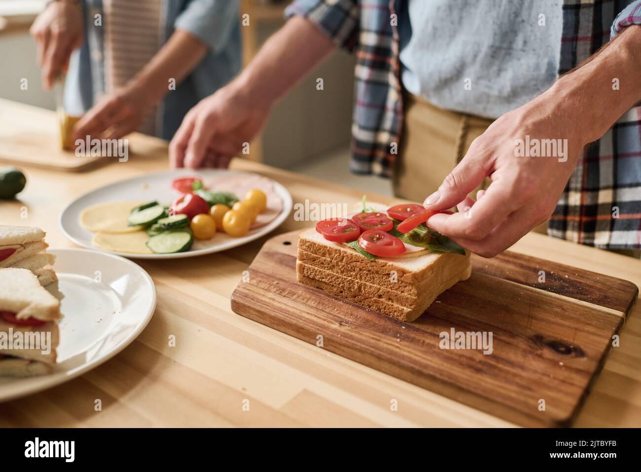Close-up of young couple cooking sandwiches with vegetables for breakfast together at table Stock Photo