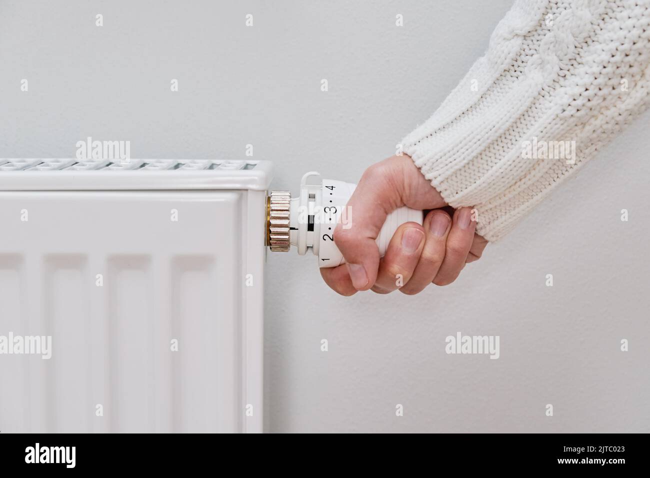 Woman adjusting temperature on heating radiator, Energy crisis concept in Europe, Rising costs in private households for gas bill due to inflation and war Stock Photo